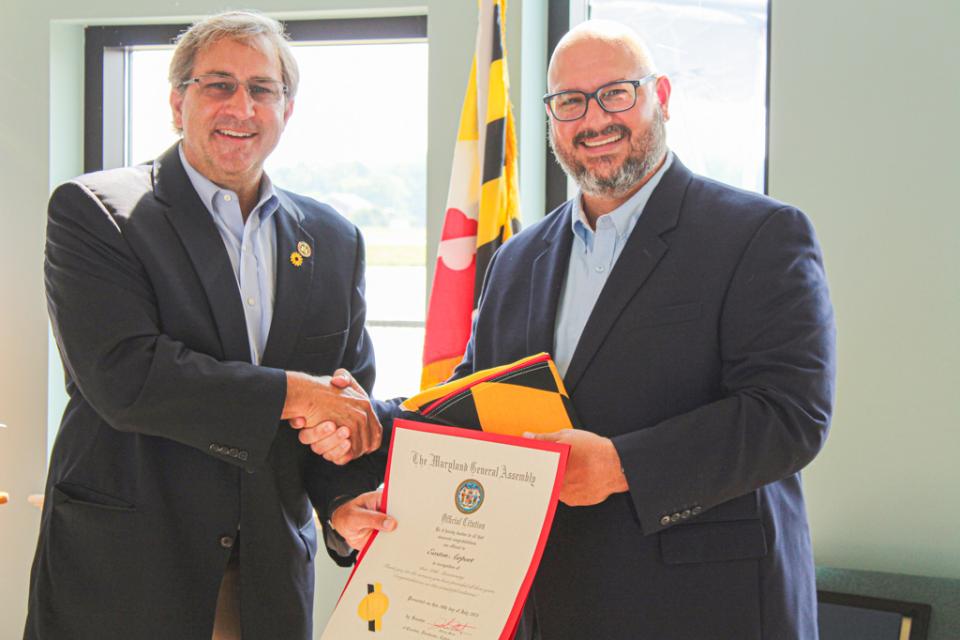 Maryland State Senator Johnny Mautz shakes hands with Micah Risher, Manager at Easton Airport after presenting an official Maryland Senate Resolution and a Maryland flag.